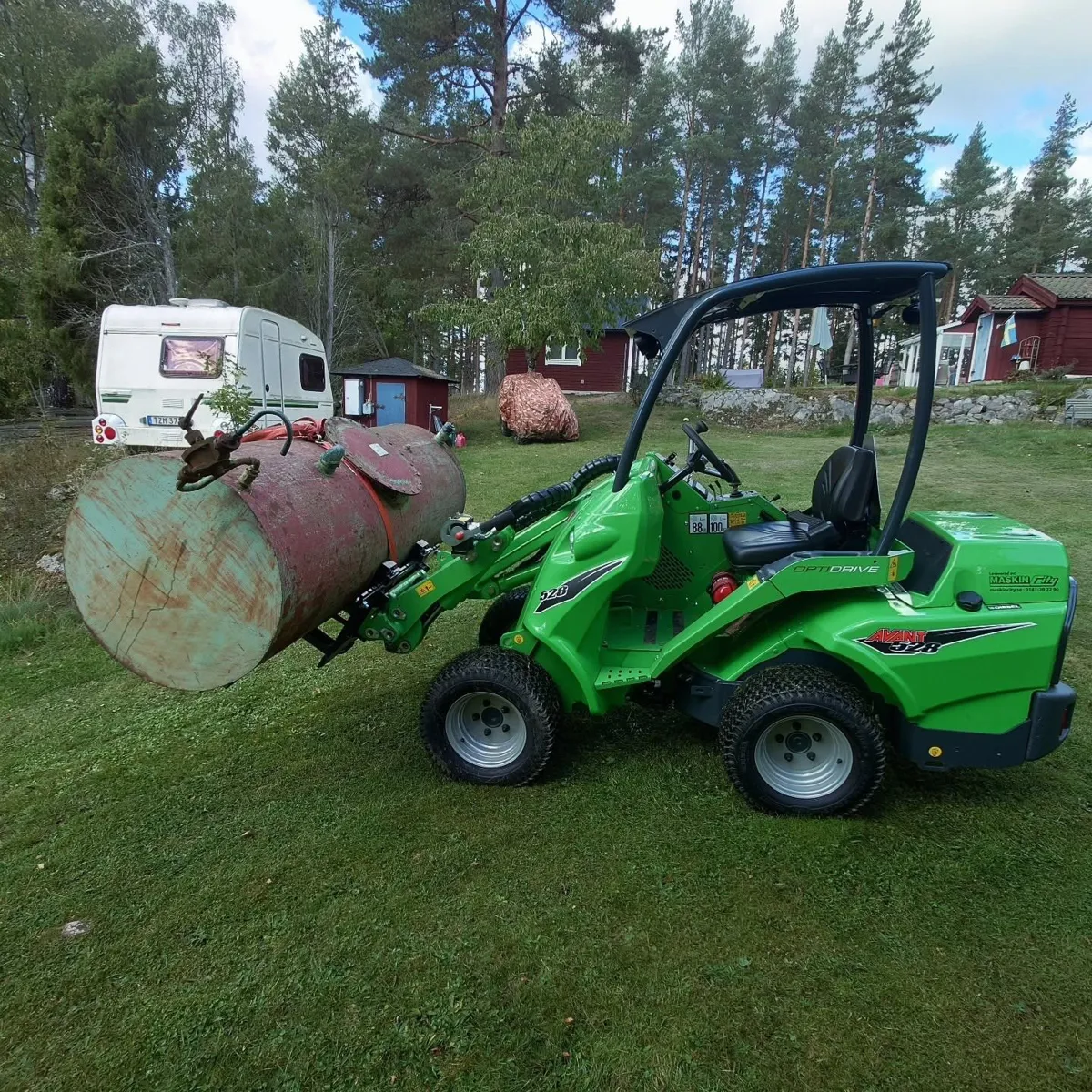 Avant 528 lyfter en gammal tank på en gräsmatta vid stugor