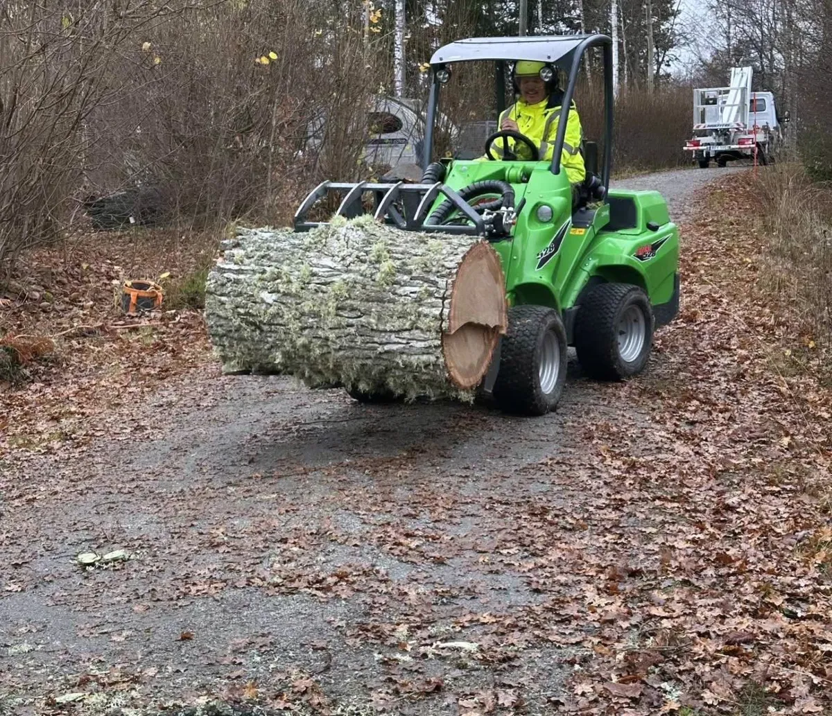 Avant-kompaktlastare bär en grov ekstock längs en grusväg